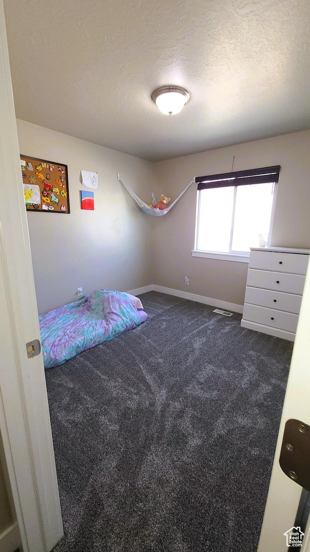 unfurnished bedroom with baseboards, dark colored carpet, a textured ceiling, and visible vents