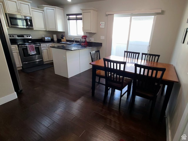 kitchen with dark countertops, a sink, a peninsula, appliances with stainless steel finishes, and dark wood-style floors