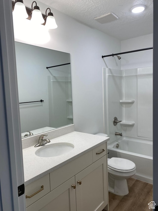 full bathroom with a textured ceiling, toilet, bathtub / shower combination, wood finished floors, and vanity