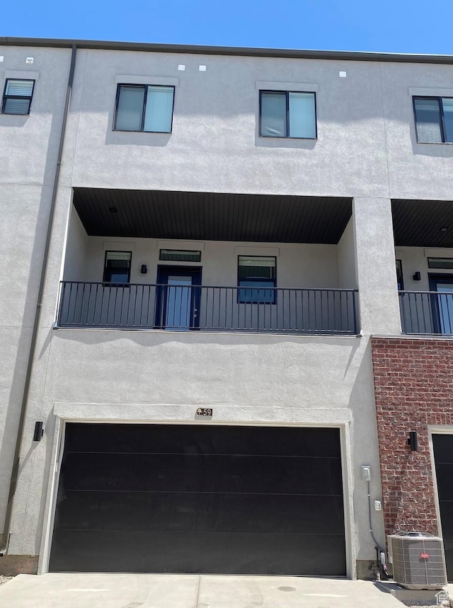 back of house featuring an attached garage, a balcony, cooling unit, and stucco siding