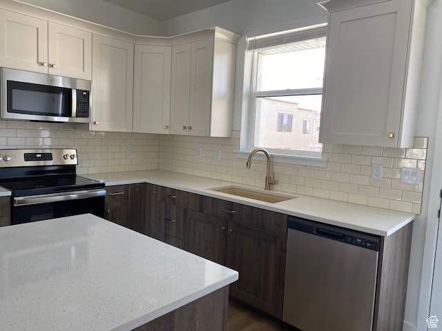kitchen with stainless steel appliances, a sink, light stone counters, and tasteful backsplash