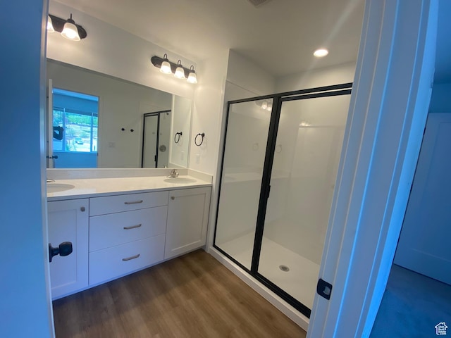 full bathroom featuring double vanity, wood finished floors, a stall shower, and a sink