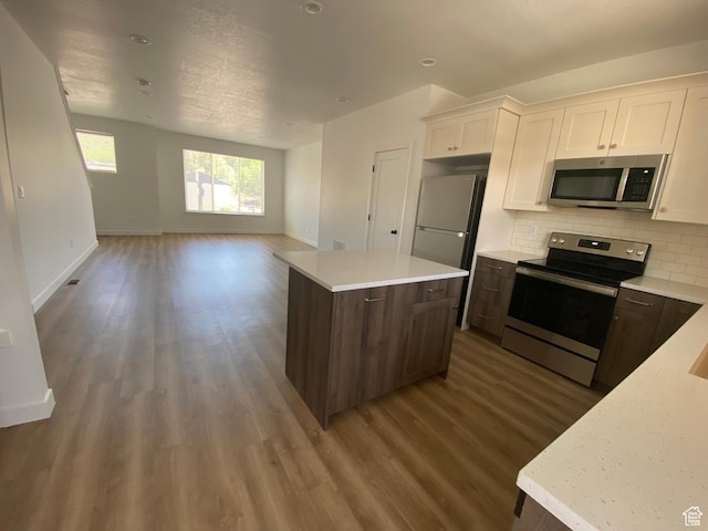 kitchen with stainless steel appliances, backsplash, wood finished floors, a center island, and baseboards