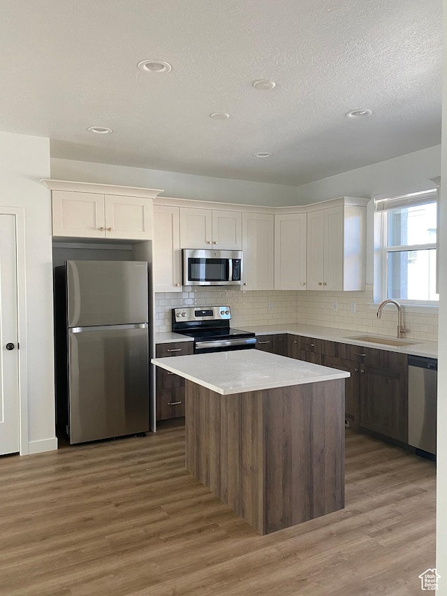 kitchen with a sink, light wood-style flooring, backsplash, appliances with stainless steel finishes, and a kitchen island