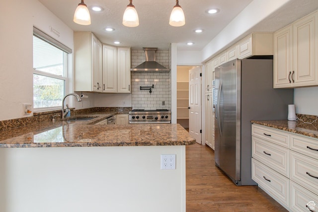 kitchen with wood finished floors, wall chimney range hood, a sink, a peninsula, and range