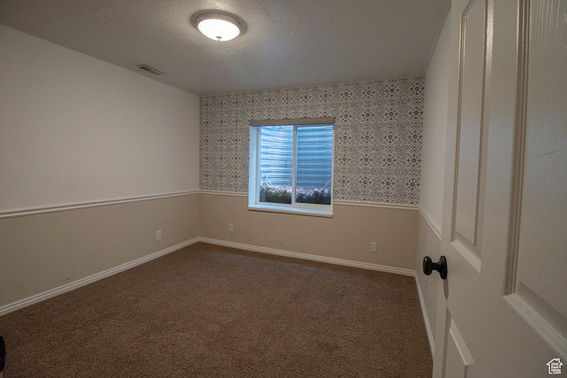 spare room featuring wallpapered walls, dark colored carpet, visible vents, and baseboards