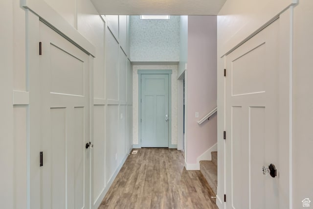 corridor featuring light wood-style flooring, baseboards, and stairs