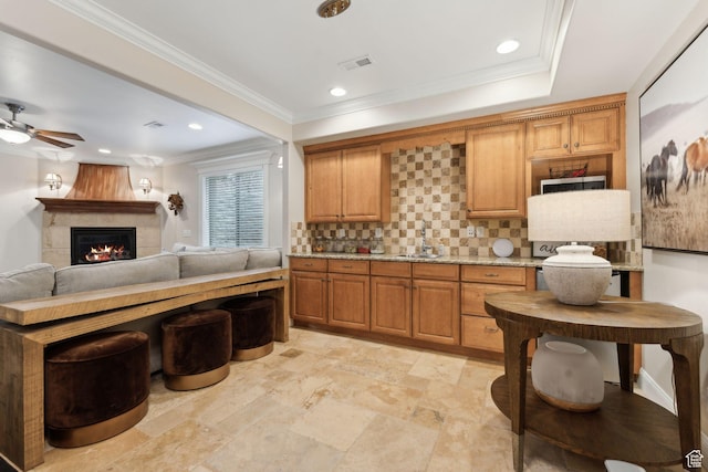 kitchen with tasteful backsplash, a sink, a warm lit fireplace, ceiling fan, and visible vents