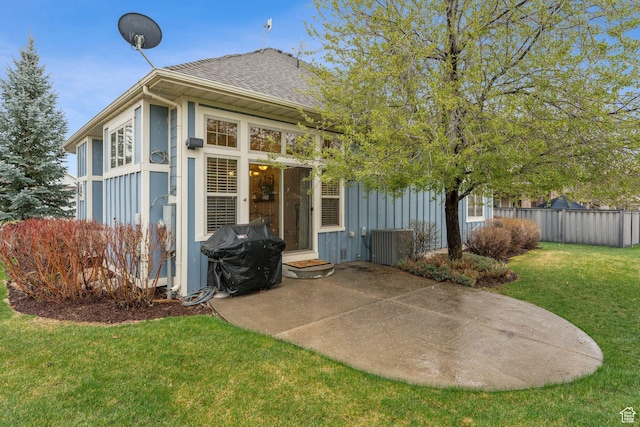 back of house featuring fence, board and batten siding, a patio area, a lawn, and roof with shingles