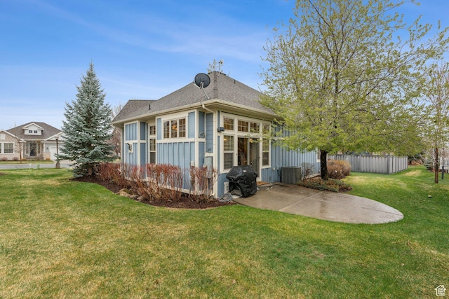 back of house featuring roof with shingles, fence, a yard, and board and batten siding