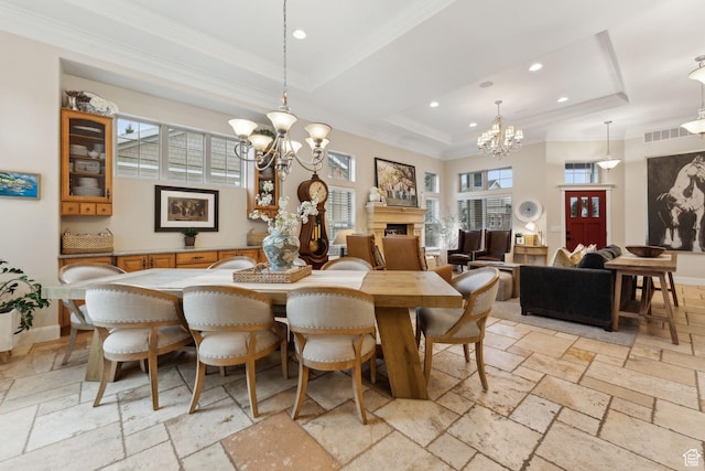 dining room with stone tile flooring, a tray ceiling, an inviting chandelier, a fireplace, and ornamental molding