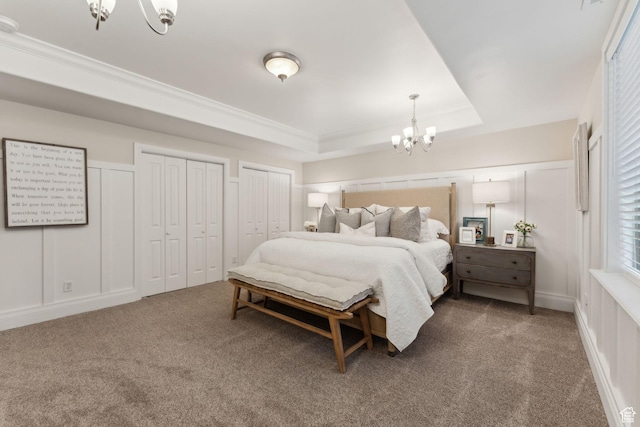 carpeted bedroom with multiple closets, a tray ceiling, a notable chandelier, and crown molding