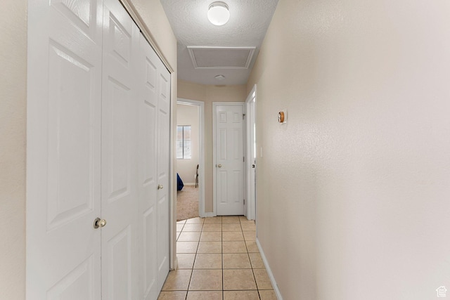 hallway with a textured ceiling, baseboards, and light tile patterned floors
