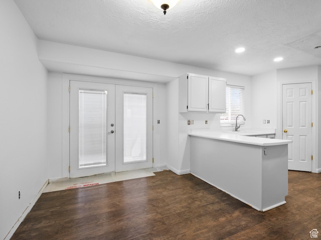 kitchen with white cabinets, a peninsula, a sink, a textured ceiling, and light countertops