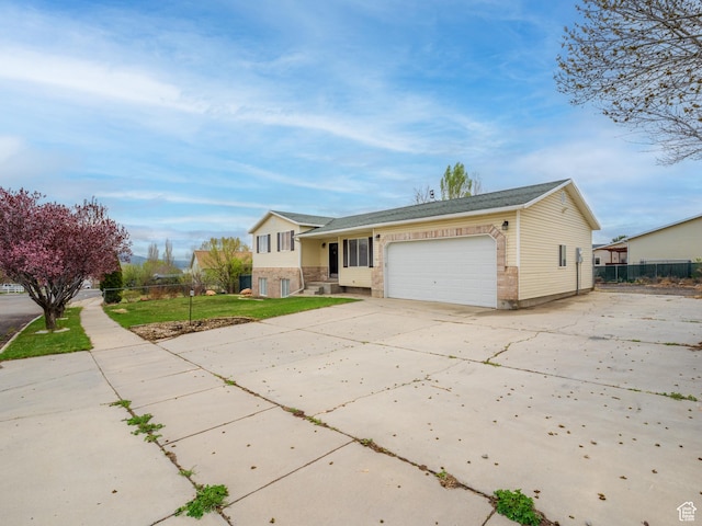 split level home with fence, a front lawn, concrete driveway, brick siding, and a garage