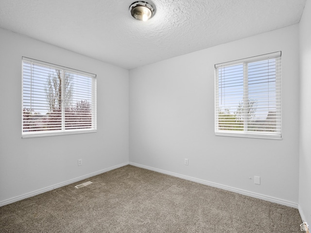 unfurnished room with baseboards, carpet flooring, a textured ceiling, and visible vents