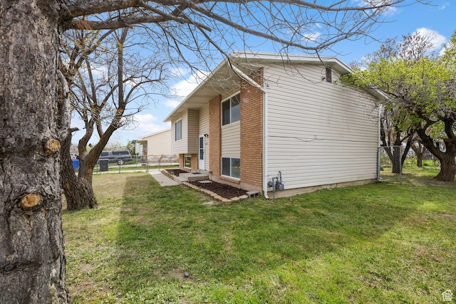 view of property exterior featuring brick siding, a lawn, and fence