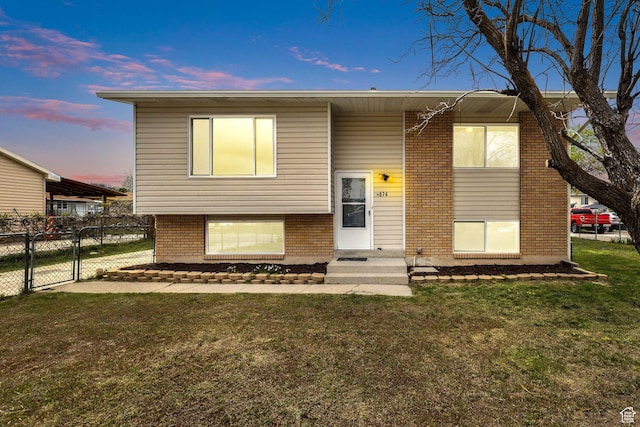 bi-level home featuring a gate, brick siding, fence, and a front yard