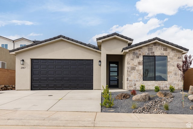 view of front of property featuring concrete driveway, stone siding, a tiled roof, an attached garage, and stucco siding