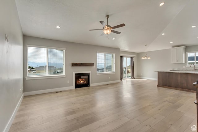 462 S 1430 E Unit 114, Tooele, UT 84074 - unfurnished living room featuring light wood-style flooring, a sink, baseboards, a glass covered fireplace, and ceiling fan with notable chandelier