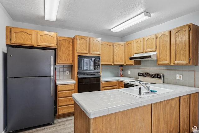 kitchen with a peninsula, decorative backsplash, under cabinet range hood, and black appliances