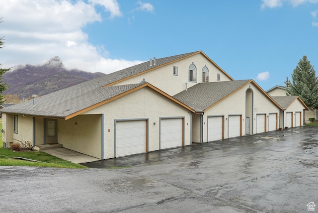 view of front facade with a shingled roof, community garages, and stucco siding