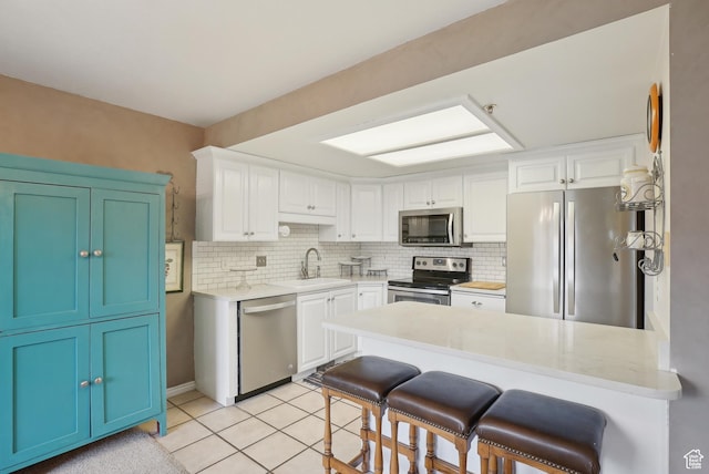kitchen with a kitchen breakfast bar, stainless steel appliances, light tile patterned floors, a sink, and a peninsula