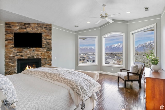 bedroom with lofted ceiling, a stone fireplace, visible vents, wood-type flooring, and baseboards