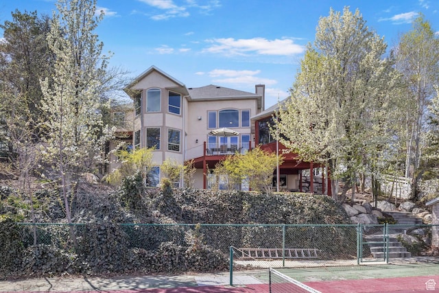 back of house featuring fence, stucco siding, and a tennis court