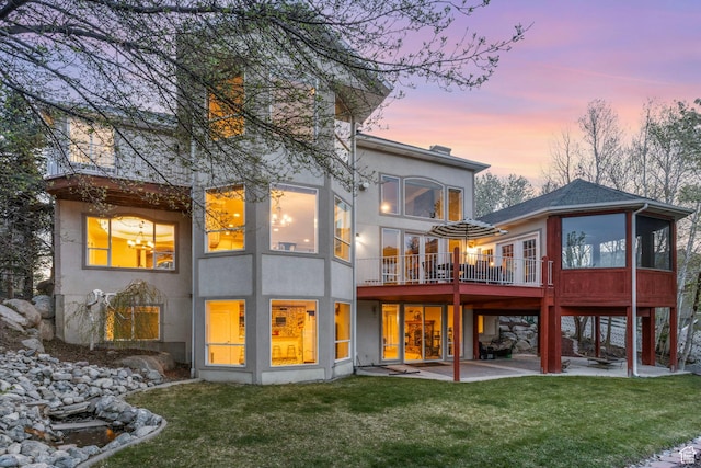 rear view of house with stucco siding, a patio, and a lawn