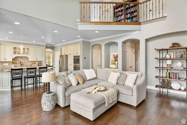 living room featuring arched walkways, baseboards, ornamental molding, dark wood-style floors, and recessed lighting