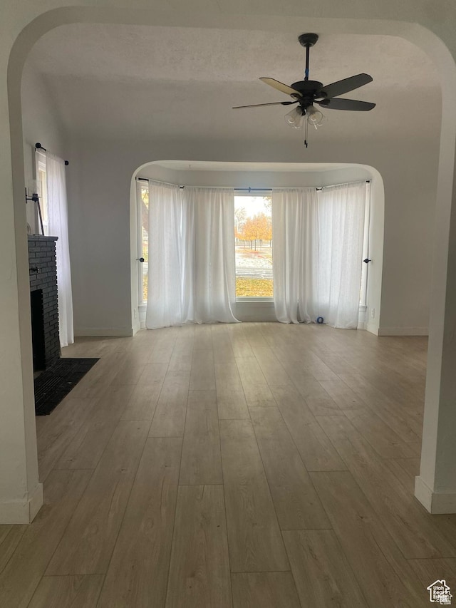 unfurnished living room with arched walkways, wood finished floors, a ceiling fan, and baseboards