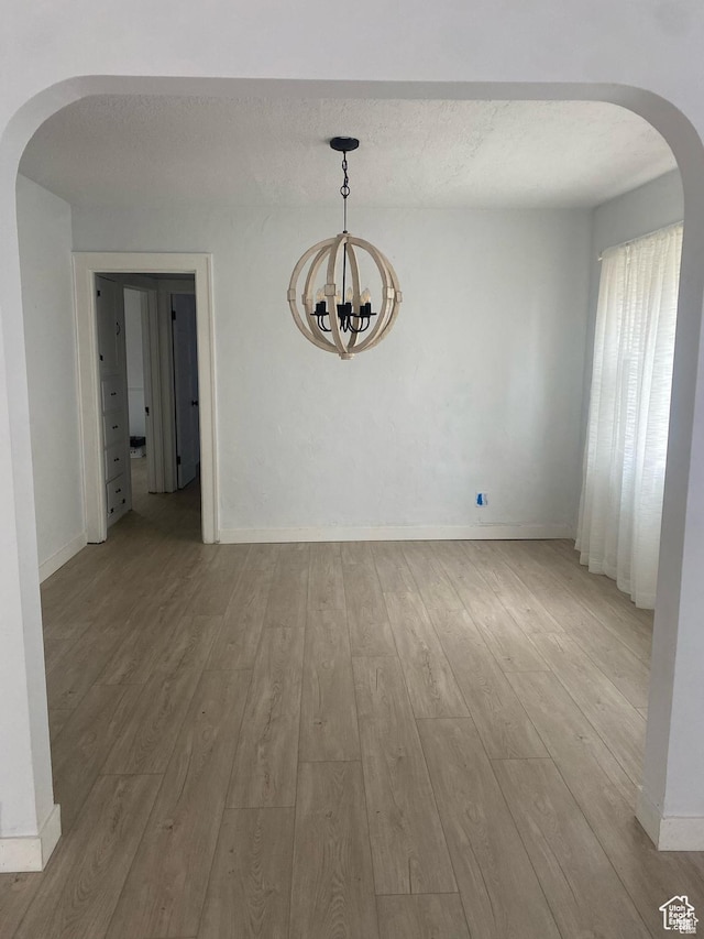 unfurnished dining area with baseboards, arched walkways, wood finished floors, and an inviting chandelier