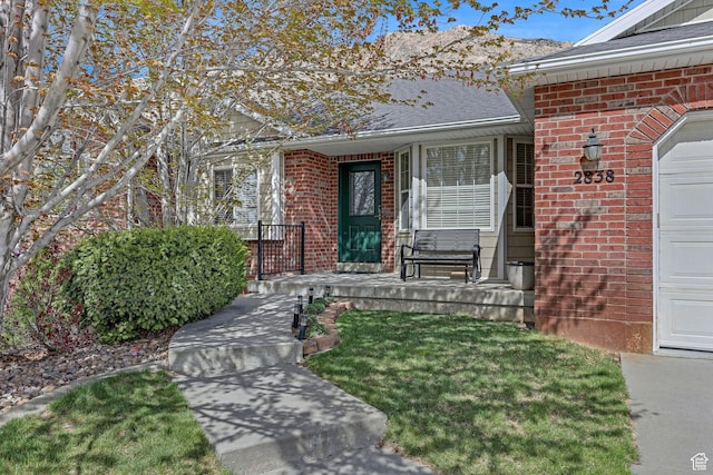 entrance to property with a lawn, brick siding, a garage, and covered porch