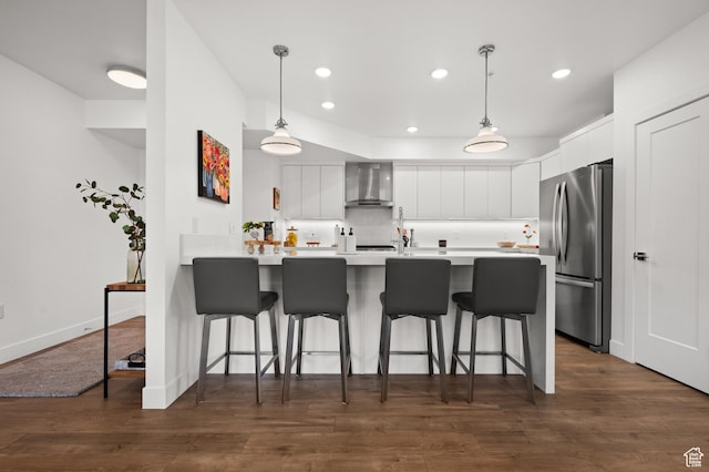 kitchen with wall chimney range hood, a kitchen breakfast bar, white cabinets, a peninsula, and freestanding refrigerator