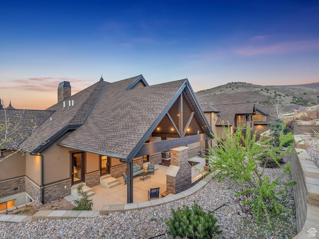 15146 S Secret Canyon Cir, Herriman, UT 84096 - rear view of house with roof with shingles, stone siding, a chimney, a patio area, and stucco siding
