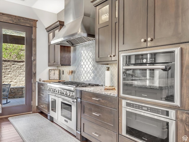 15146 S Secret Canyon Cir, Herriman, UT 84096 - kitchen featuring wall chimney exhaust hood, backsplash, glass insert cabinets, wood finished floors, and appliances with stainless steel finishes