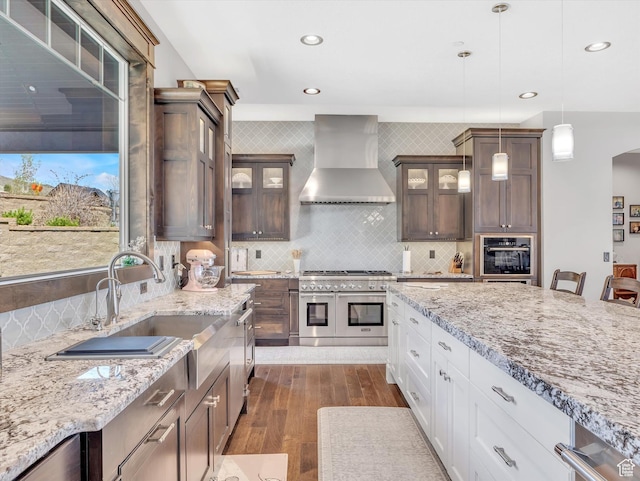 15146 S Secret Canyon Cir, Herriman, UT 84096 - kitchen featuring dark wood-style floors, light stone counters, stainless steel appliances, wall chimney range hood, and a sink