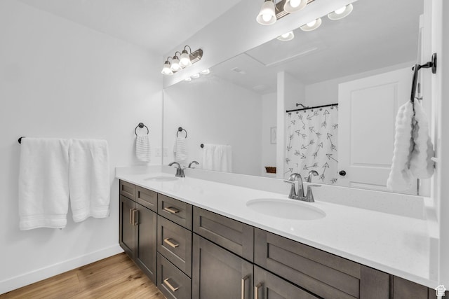 full bath featuring baseboards, wood finished floors, a sink, and double vanity