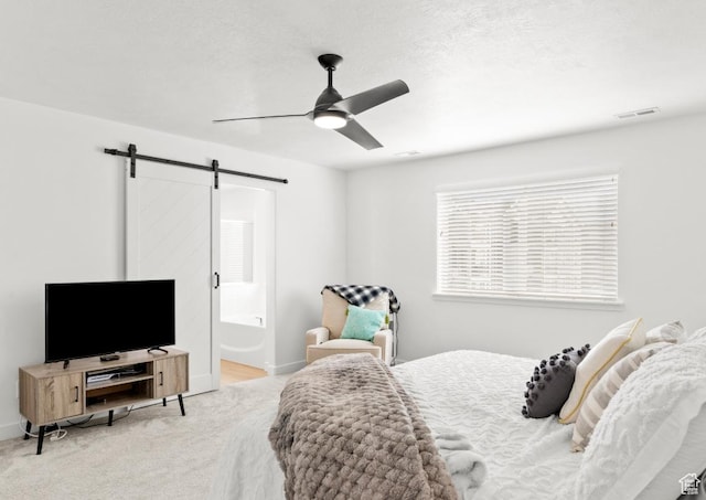 carpeted bedroom featuring a barn door, a ceiling fan, connected bathroom, baseboards, and visible vents