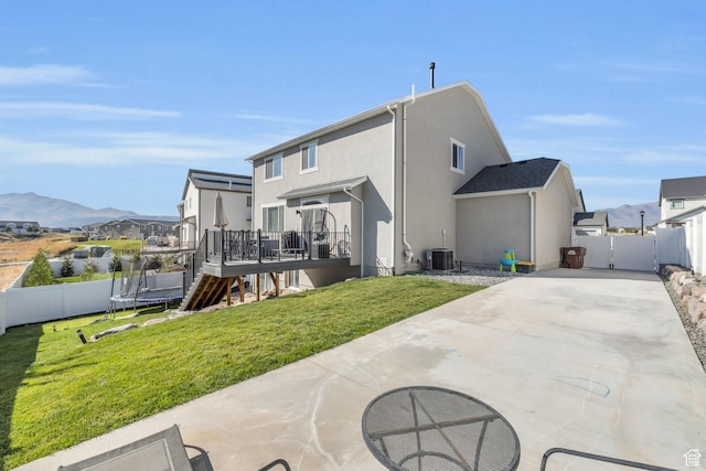 rear view of house featuring central AC unit, a trampoline, a deck with mountain view, a fenced backyard, and a patio