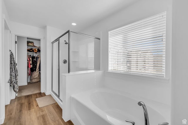 bathroom with a spacious closet, wood finished floors, a garden tub, and a stall shower