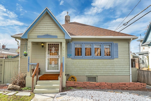 bungalow featuring fence, a shingled roof, and a chimney