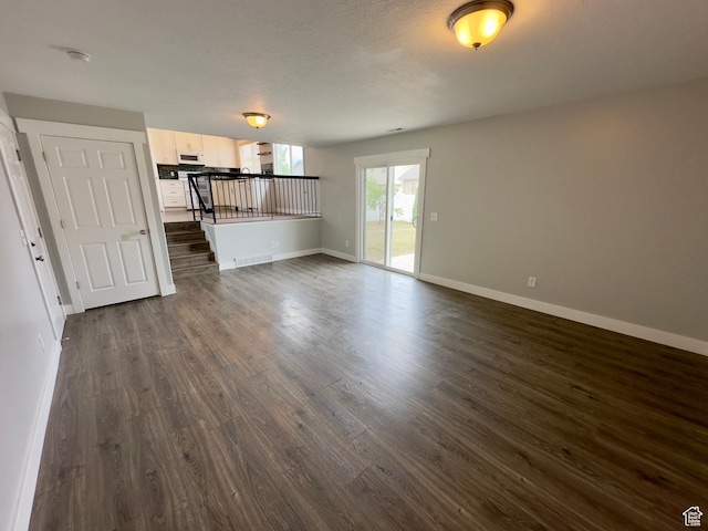 unfurnished living room featuring dark wood finished floors, baseboards, and stairway
