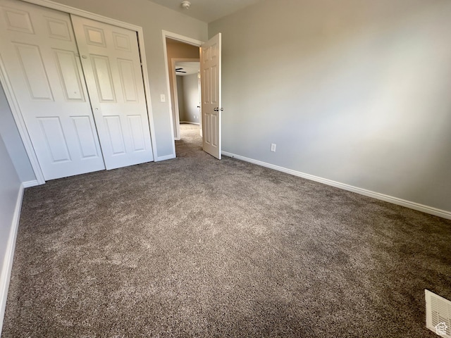 unfurnished bedroom with dark carpet, baseboards, and a closet