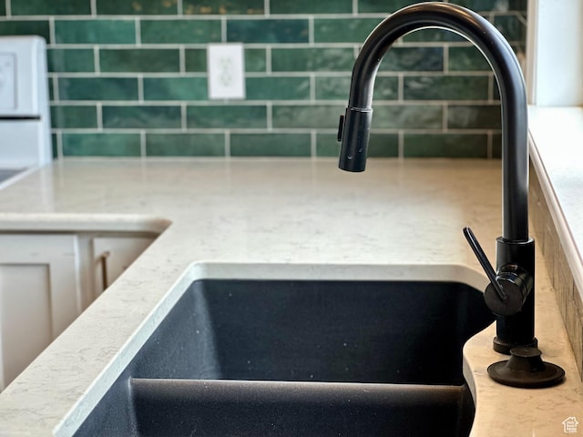 kitchen view of a sink, backsplash, white cabinetry, and light countertops