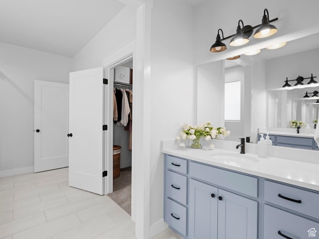 bathroom with vanity, a walk in closet, and baseboards