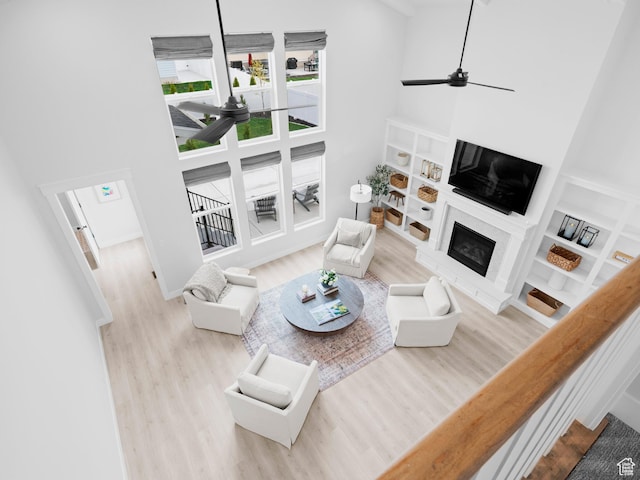 living area with a towering ceiling, a ceiling fan, wood finished floors, a glass covered fireplace, and baseboards