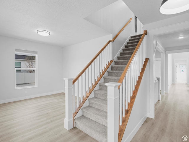 stairway featuring wood finished floors, baseboards, and a textured ceiling