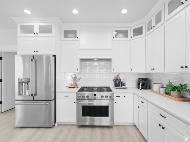 kitchen featuring high end appliances, light countertops, backsplash, light wood-style flooring, and recessed lighting